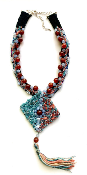 A handcrafted Sunset Mirage Tassel Necklace with Carnelian Agate centerpiece, Blue Chalcedony chips and beads, glass seed beads, and a suede tassel.