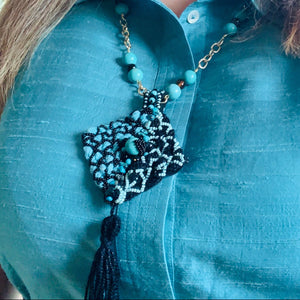 Person wearing a blue shirt with a decorative necklace featuring beads and tassels.